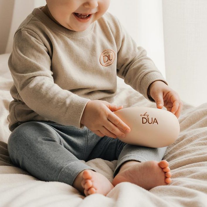 Hand hält einen runden, rosa Silikonlöffel und ein Spielzeug mit Hasenohren.