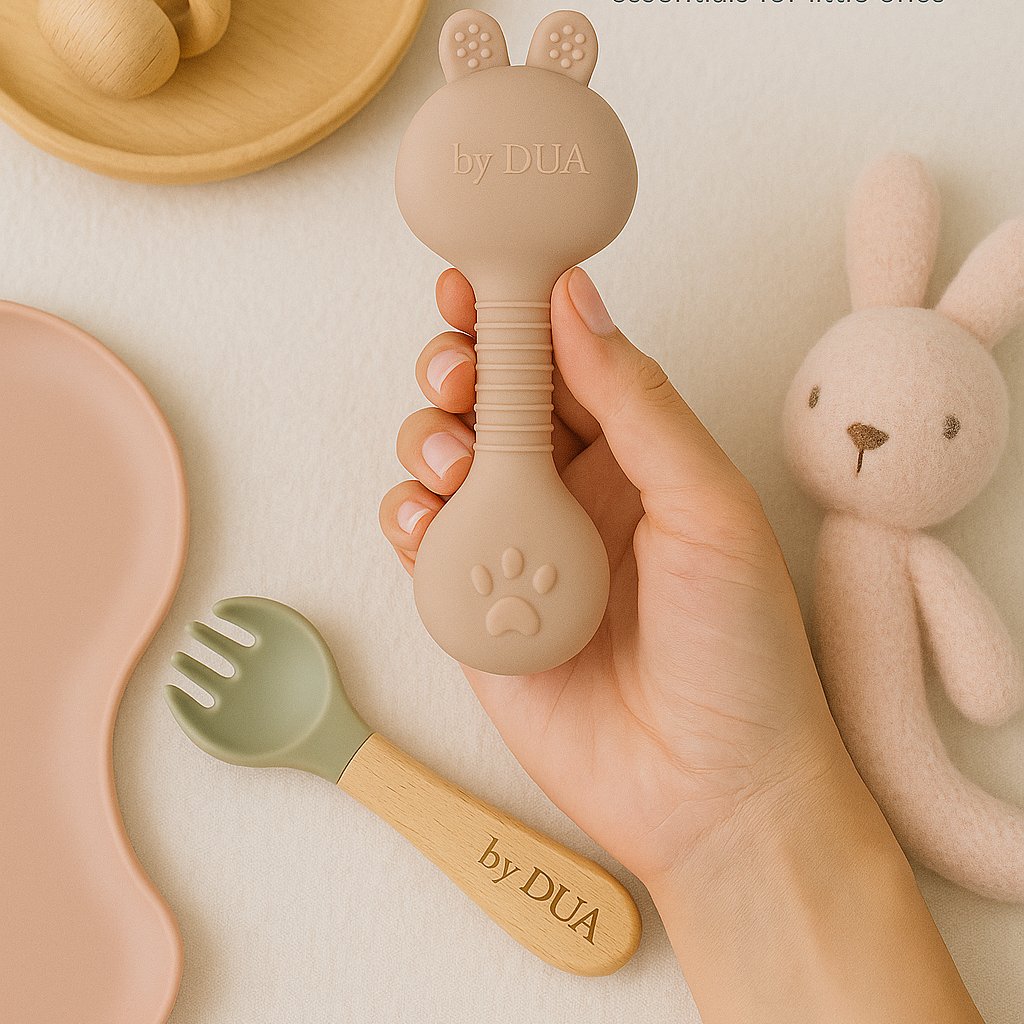 Hand hält einen runden, rosa Silikonlöffel und ein Spielzeug mit Hasenohren.